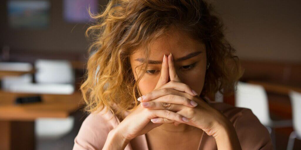 A woman with her hands folded in front of her face, facing burnout.